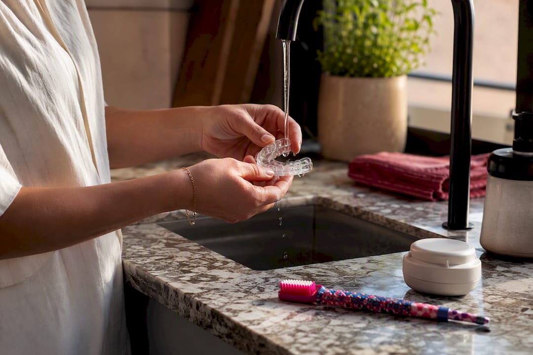 Hands rinsing night guard over sink